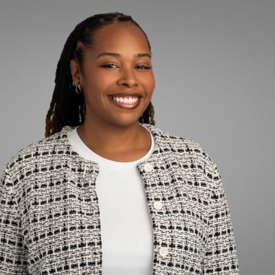 Portrait of Janelle Flowers, smiling, with long, dark hair, and a grey checked cardigan.