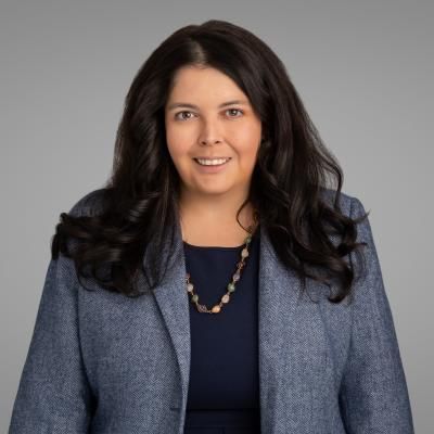 Portrait of Renee Williams, smiling, with long, dark hair, wearing a grey jacket.